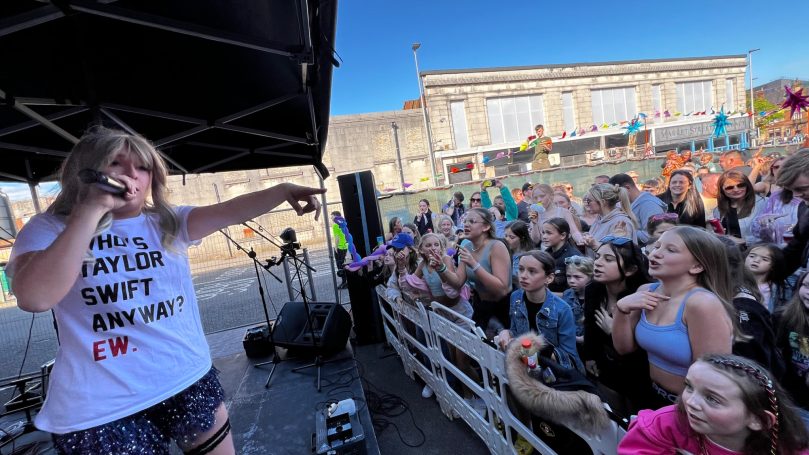 Singer performing on stage with an enthusiastic crowd engaged in the background.