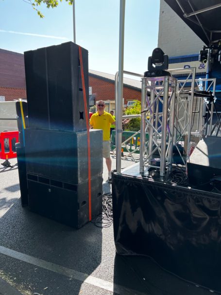 A man in a yellow shirt stands near large speakers on a stage setup.